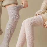 Two models wearing cozy, textured over-the-knee socks in light beige and pale pink, shown against a warm neutral background.
